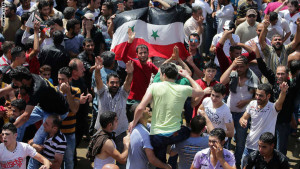 Men holding a Syrian flag dance near the Syrian Embassy in Yarze east of Beirut on May 28, 2014. Filling the streets around the embassy in Beirut, thousands of Syrians turned out to vote in a controversial presidential election that Bashar al-Assad is expected to clinch effortlessly, as civil war rages. AFP PHOTO/ JOSEPH EID (Photo credit should read JOSEPH EID/AFP/Getty Images)